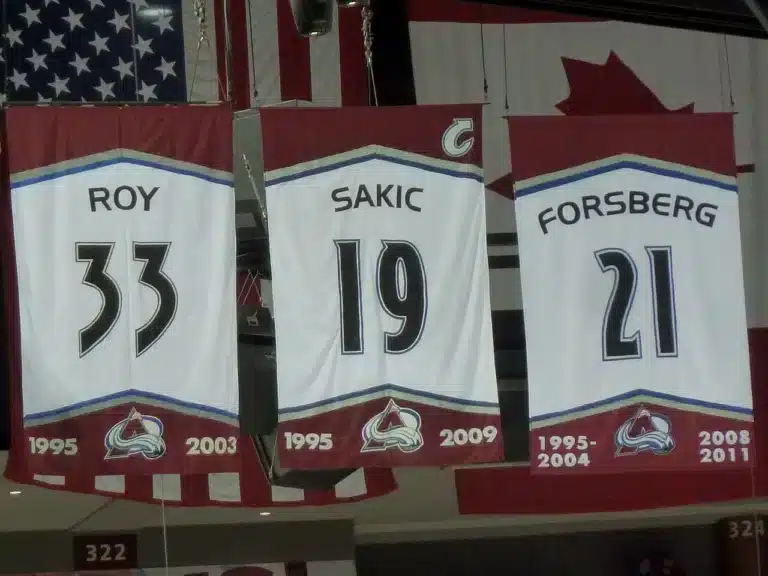 Colorado Avalanche retired jersey banners for Roy 33, Sakic 19 and Forsberg 21 hanging from the arena rafters, a reminder of the standard amid the Colorado Avalanche struggles.